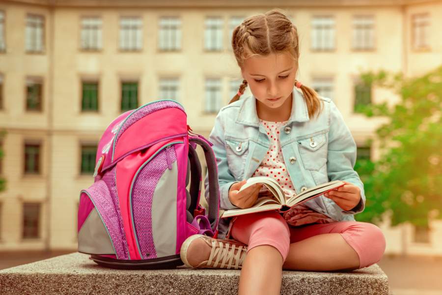 petite fille qui lit a côté de son sac d'école